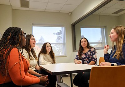 Five individuals seated at a table in an observation room with large glass window behind them