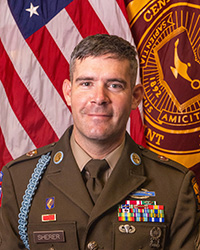 Closeup image of SFC Neill Sherer wearing his military uniform with the American and Central Michigan University flags behind him.