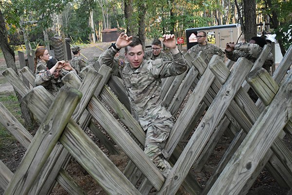 An Army ROTC student wearing a green camouflage steps between wooden beams at the Field Leaders Reaction Course