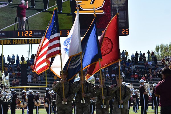 Four Army ROTC cadets hold flags while standing on the Central Michigan University football field before a game.