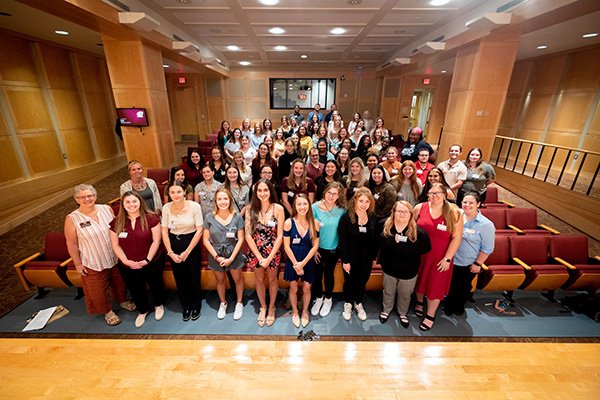 Students and faculty at the annual Social Work Convocation Ceremony all standing and looking up at the camera in the front of the auditorium.