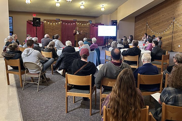 Social Work faculty member Valerie Austin stands at a podium speaking to dozens of community members seated in chairs