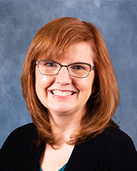 Jennifer Schisa in a dark jacket and glasses smiling at the camera.