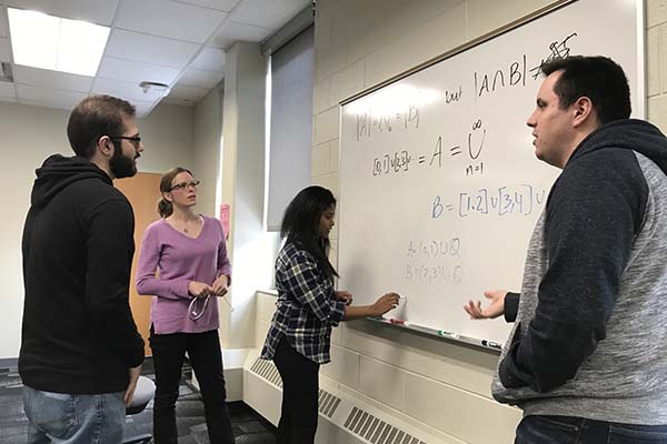 Group of students discussing a math equation on a whiteboard.