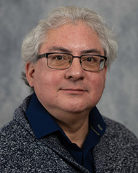 A man in glasses wearing and a grey sweater poses for a headshot.