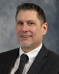 A man wearing a suit coat, collared shirt and tie poses for a headshot.