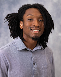 20250915_GalenRaymond_200x250 A man with dark hair and a grey shirt smiles in front of a grey background.
