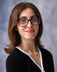 20250918_AnetaBoutros_200x250 A woman in glasses, dark hair, and a dark shirt in front of a grey background.