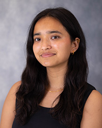 20250918_Suhani_Bam_Thakuri_200x250 A woman with dark hair and a dark shirt in front of a grey background.
