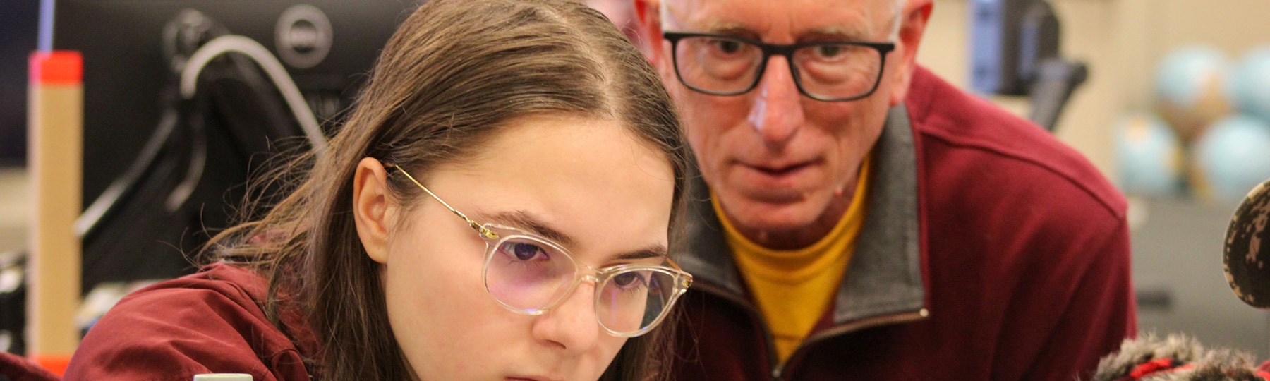 A student concentrates on her work in a lab setting, while a faculty member closely observes.
