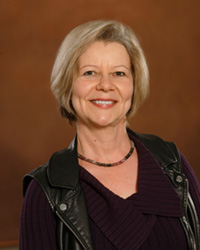 A woman wearing a black vest in front of a brown backdrop.