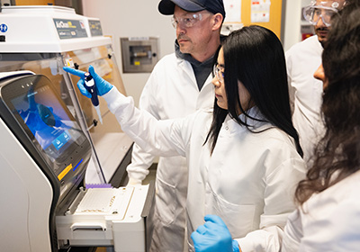 A group of students in lab coats placing samples into a machine.