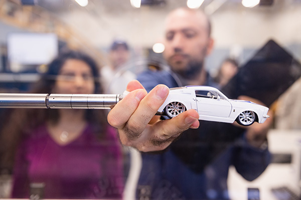 Two students placing a model car into a wind tunnel to examine the effects of airflow and aerodynamics.