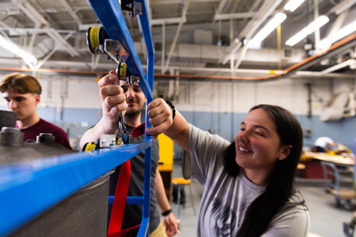 A group of students attaching brackets to a blue metal frame.