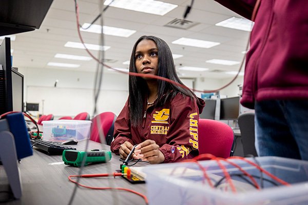 A student in a long sleeve, maroon CMU shirt and long black hair testing an electronic circuit.