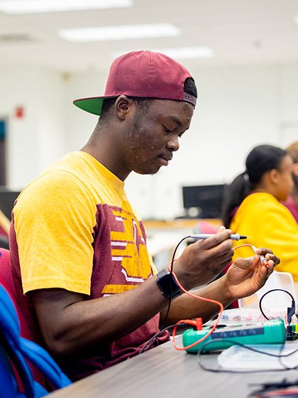 A student holding testing wires in an electronics lab.