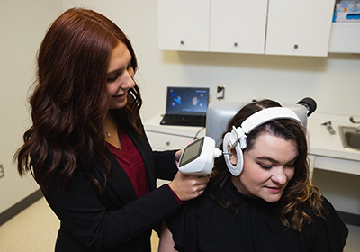 An audiology student using a device to check the ear of a patient.