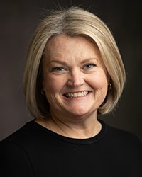 MaryBeth Smith has blonde hair and wears a black sweater while smiling for a head shot.