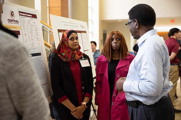 Three individuals talking next to a poster.