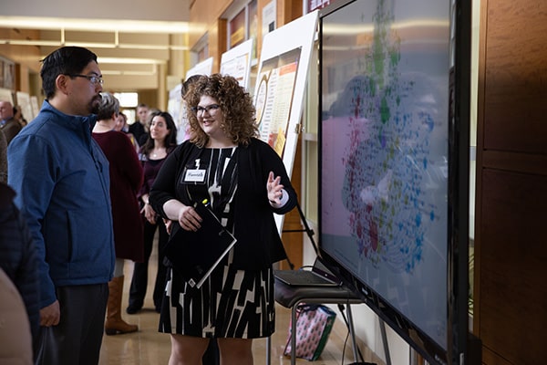 Two individuals standing in front of a large screen.