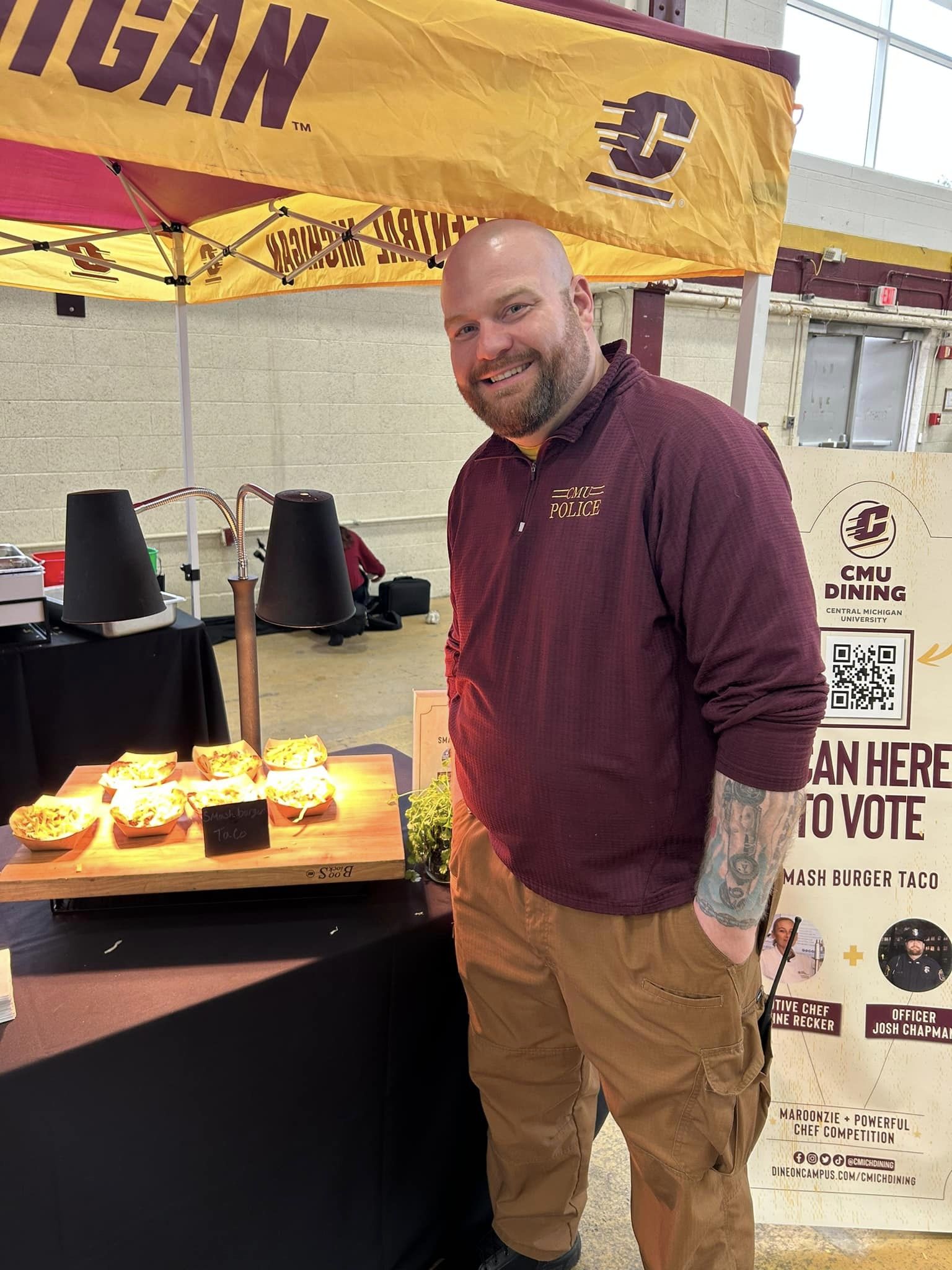 joshfoodcart Officer Josh Chapman standing by his meal creation in collaboration with Chartwell. He is under a CMU tent with low lighting.