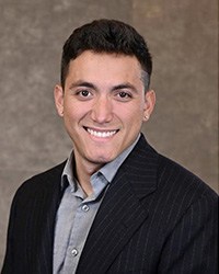 A man wearing a black suit coat poses for a headshot.