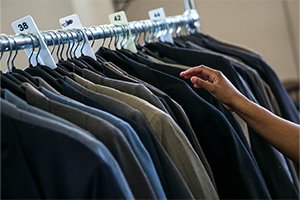 A hand reaches for a suit jacket hanging on a clothing rack.