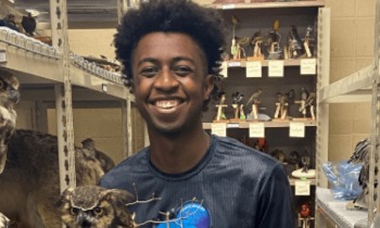 a student smiles and holds up a taxidermy owl while standing in a museum archive