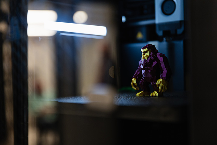 A maroon and gold-colored 3D-printed ape sits inside a 3D printer