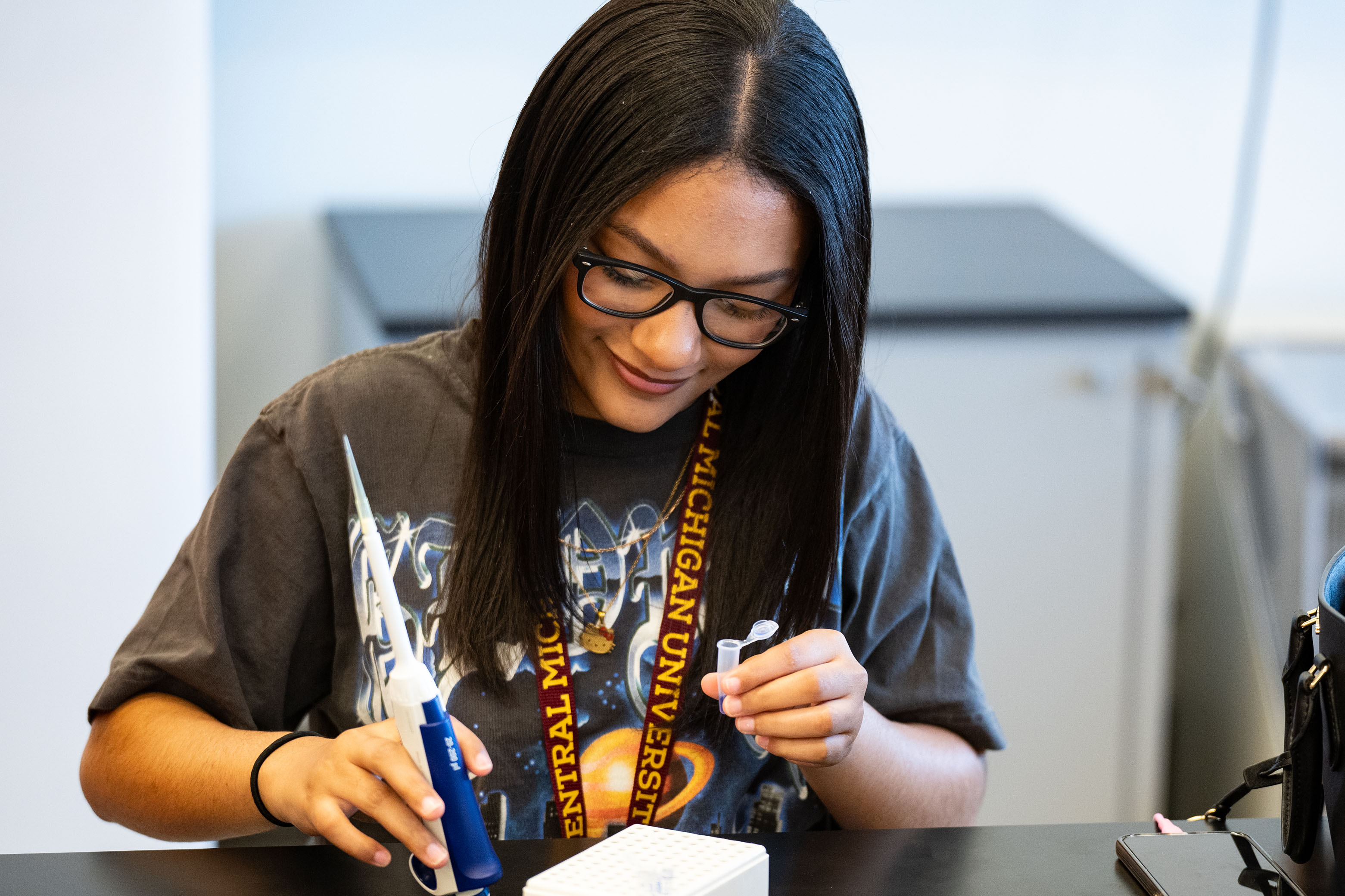 A smiling young woman wearing glasses creates a lab sample.