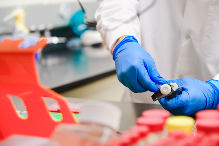 Two gloved hands hold lab samples for analysis in a lab.