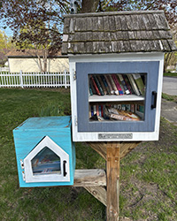 A gray square door inside a white frame sits on one level of a two-tiered stand with a white house-shaped door inside a light blue frame on the other.
