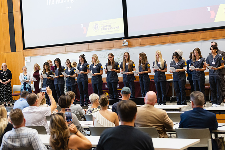 A group of nursing students standing in a row at the front of an auditorium