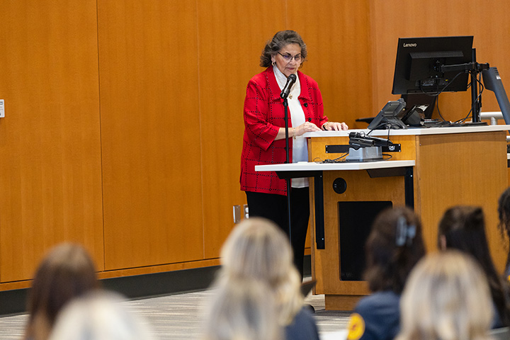 A woman in a red coat standing at a podium with a microphone