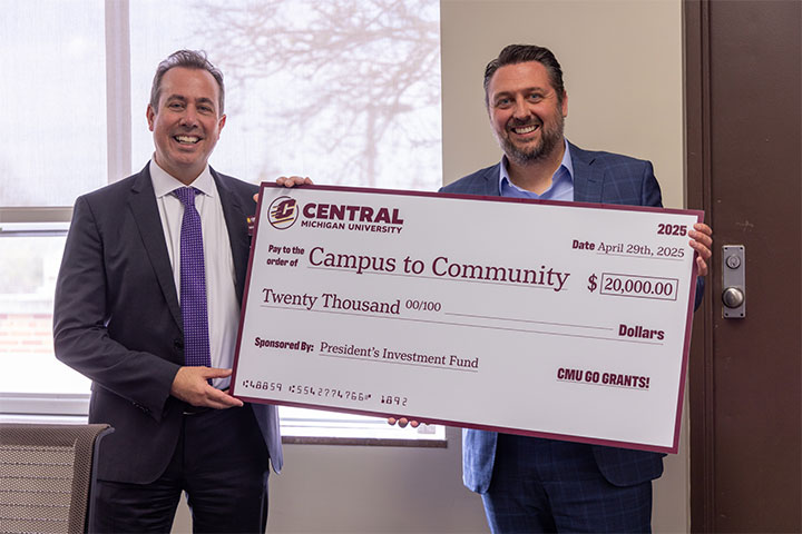 Two men stand in front of a window holding an oversize check