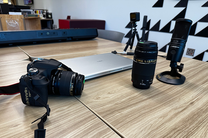 A camera, camera lens, laptop computer and microphone on a table