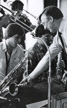 A man pointing a microphone into a saxophone as another man plays music.