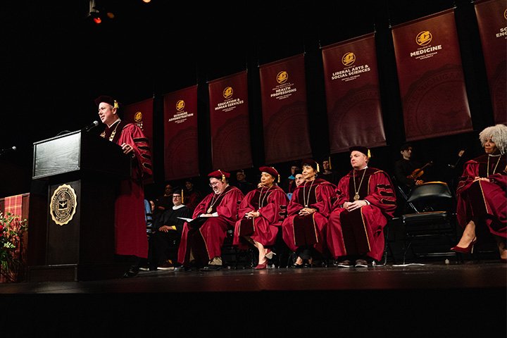 a man in red robe standing at a podium with a microphone