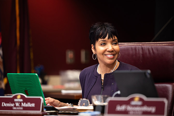 A woman wearing a purple dress sitting at a desk smiling.