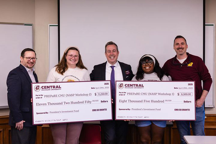 Two female students hold giant checks at an awards presentation