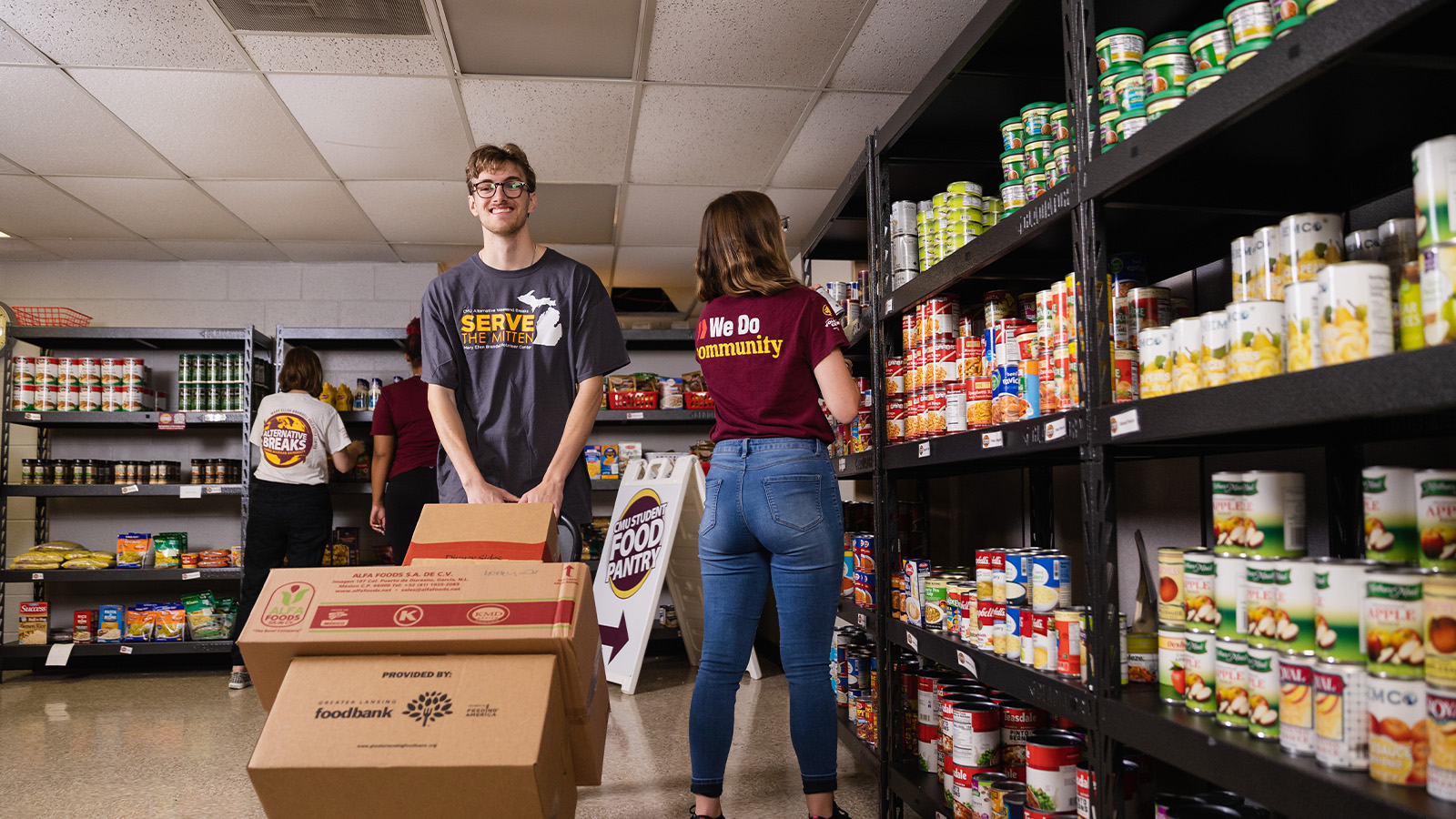 Paying Forward_Volunteer Services A student volunteering at a food pantry unloading boxes of canned goods and produce.