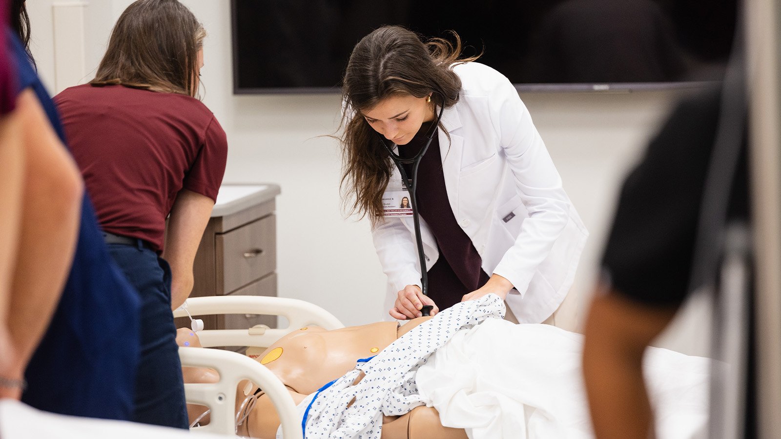 World Class_Simulator A brown haired female medical student works on a patient simulator in a hospital bed.