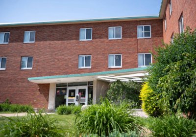 Front entrance of Merrill Hall with glass doors, white canopy, and surrounding landscaping.