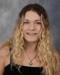 24-10-03 Jaelyn Welch Poartrait -01 Jae Welch, Graduate Assistant for Sexual Aggression Services. Black top with long blonde hair and a grey background.