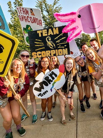Students wearing tan vests and holding signs with animal names on them.