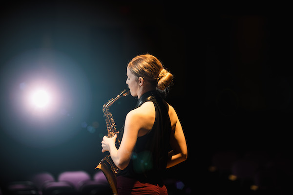 picture of the side of a student on stage in a spotlight playing saxophone