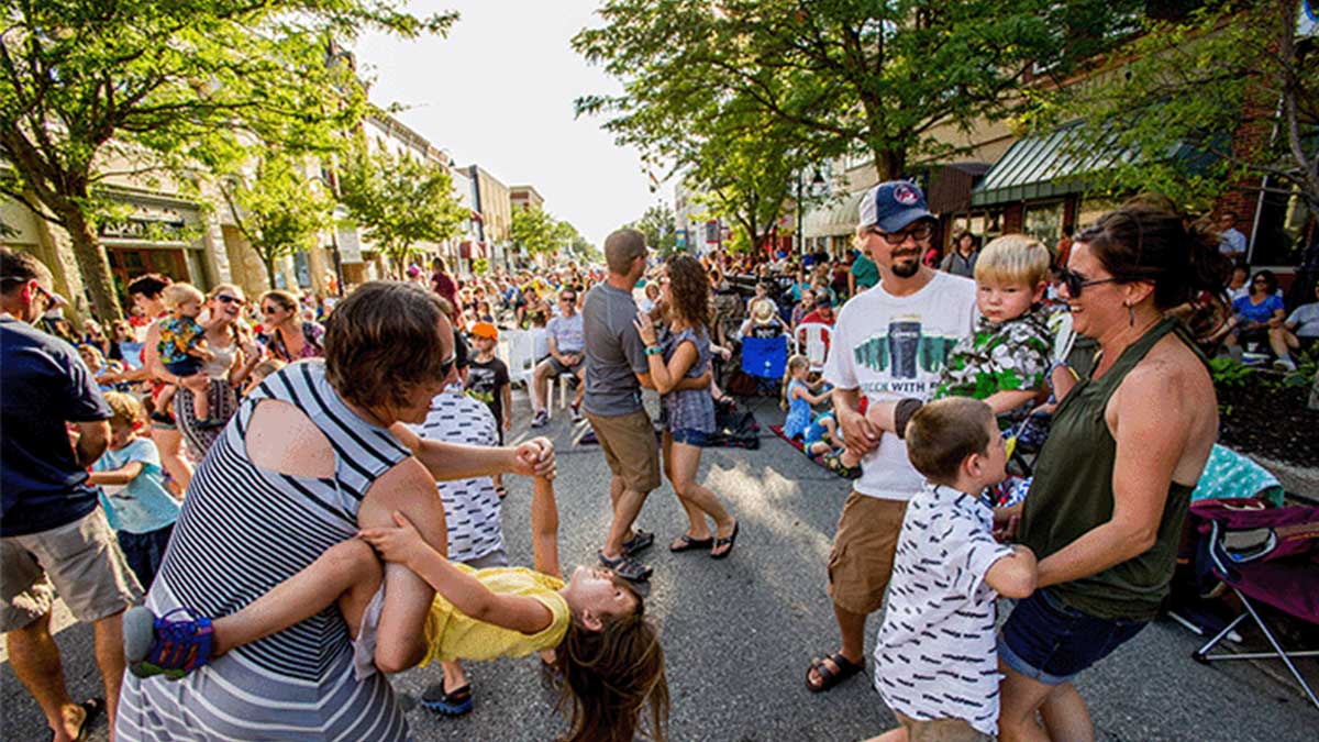 Parents and young children dance to music at an outdoor festival.