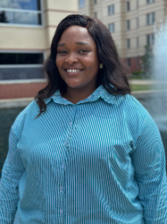A woman with dark hair wearing a blue button up smiling at camera.