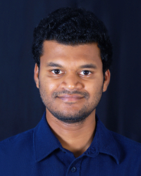 A man with dark hair wears a blue shirt and smiles for the camera.