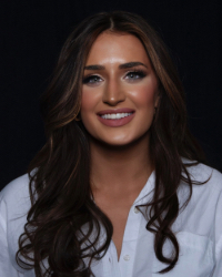 A woman with long dark brown hair smiling and wearing a white button up shirt